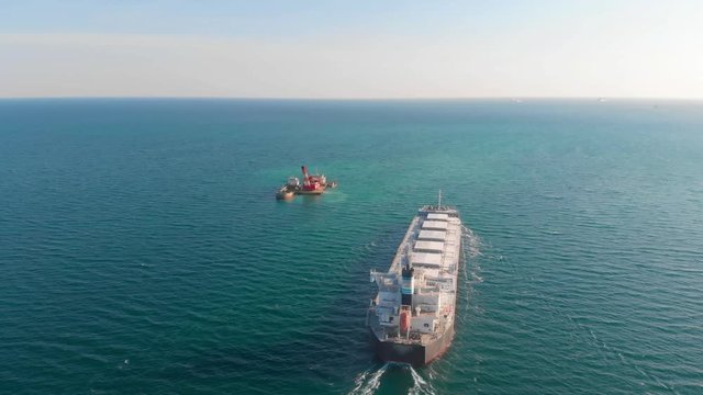 The large cargo vessel left the port after loading and moves in the right direction at high speed. Balker goes in the ocean.