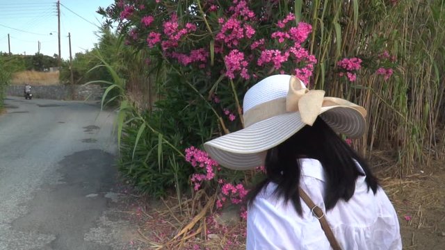 Following back of female in summery hiking outfir walking next to flowers in Greek countryside SLOW MOTION