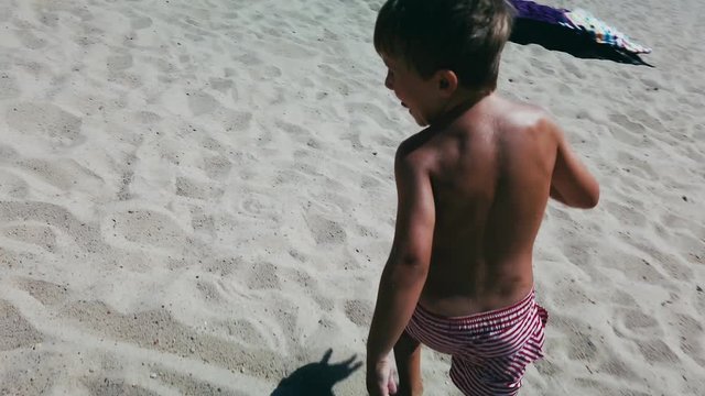 POV as camera chases little boy around on a sandy beach on summer day.