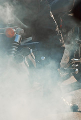 The smoke comes out from under the wheels. Motorcycle wheel closeup. Smoke due to tire rubbing against asphalt. The rider prepares to do the trick on the motorcycle. Burned rubber on the road.