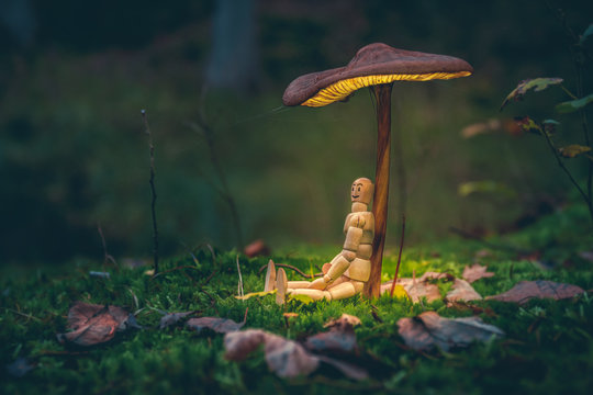 Wooden Mannequin Sitting Under A Mushroom. Miniature Figure, Human Representation In The Forest. Nature, Environment Concept