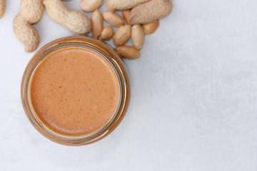 Creamy peanut butter in jar and peanuts.