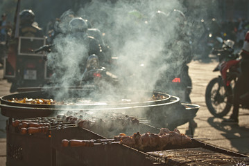 Grilled meat in a large frying pan. Grilled vegetables on motorcycle festival background. Blurred motorcycles in the background. Parking for bikers. Motorcycle food interchange.