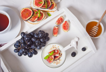 Yogurt with muesli and fig fruit in a glass, sandwich with cream cheese, figs and honey on the white treay. Healthy food concept.