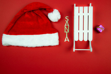 Czapeczka Św. Mikołaja oraz napis Santa oraz białe sanki na czerwonym tle - obrazy, fototapety, plakaty
