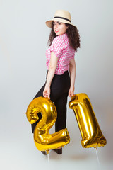 The girl in the hat holds balloons that show the numbers 21. Her birthday.