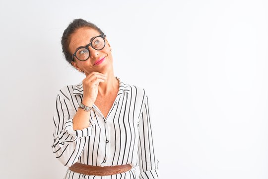 Middle age businesswoman wearing striped dress and glasses over isolated white background with hand on chin thinking about question, pensive expression. Smiling with thoughtful face. Doubt concept.