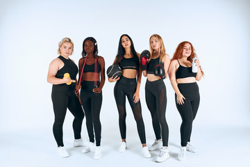 Fototapeta premium Sportowe dziewczyny w sporcie na sobie stanąć wraz z rękawicami bokserskimi, hantlami i innymi sportowymi rzeczami, spojrzeć na aparat na białym tle, białe tło