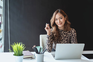 Charming asian businesswoman sitting working on laptop in office. Looking at camera.