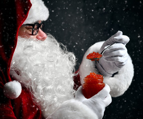Santa Claus eating holding spoonful of red caviar fish salmon under snow. New year and Merry...