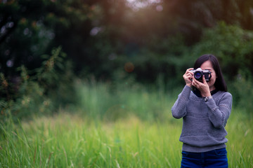 Beautiful asian woman taking picture with analog film camera in green natural background.
