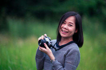 Beautiful asian woman taking picture with analog film camera in green natural background