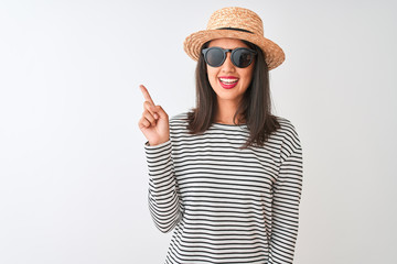 Chinese woman wearing striped t-shirt hat sunglasses standing over isolated white background with a big smile on face, pointing with hand and finger to the side looking at the camera.