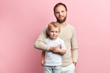 father and son looking at the camera while standing , happy fatherhood, parenthood. isolated pink...