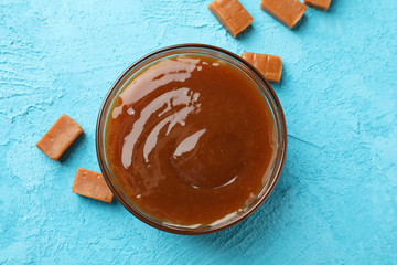 Glass jar with salted caramel and candies on blue background, top view