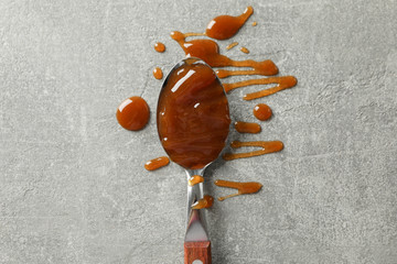 Spoon with caramel on grey background, space for text