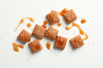 Salted caramel candies and sauce on white background, space for text