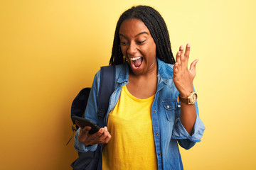 African american student woman using smartphone standing over isolated yellow background very happy...