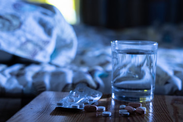 some of medicine pills and a glass of water  on a nightstand next to the bed at night, treatment insomnia concept