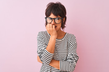 Young beautiful woman wearing striped t-shirt and glasses over isolated pink background looking stressed and nervous with hands on mouth biting nails. Anxiety problem.