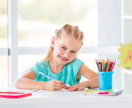 Cute kid girl sitting at the desk, coloring with pencils