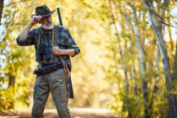 Bearded caucasian man in hunting clothes stand looking away. Forest background