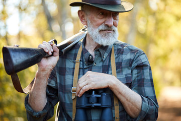 Portrait of open-minded senior hunter with gun on shoulders