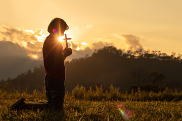 Silhouette of woman praying with cross in nature sunrise background, Crucifix, Symbol of Faith. Christian life crisis prayer to god.