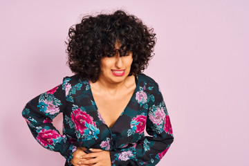 Young arab woman with curly hair wearing floral dress over isolated pink background with hand on stomach because nausea, painful disease feeling unwell. Ache concept.