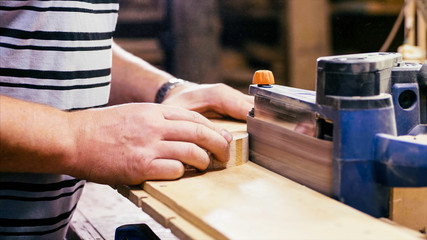 Closeup hands of male carpenter worker is grinds the wood detail. Craftsman polishing with grinding machine at wood workshop.