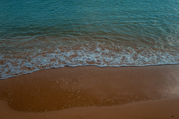 Waves crashing on the sand at the seashore with blue sea