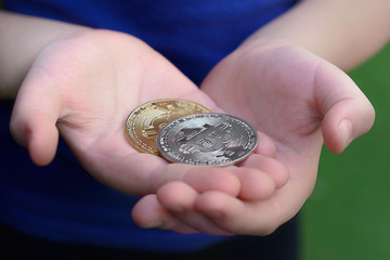 Child holds in open palms gold and silver bitcoins, close up