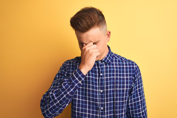 Young handsome man wearing casual shirt standing over isolated yellow background tired rubbing nose and eyes feeling fatigue and headache. Stress and frustration concept.