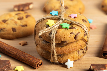 Close-up of chocolate chip cookies on a wooden Board with sprinkles and tied rope, next to chocolate and cinnamon sticks