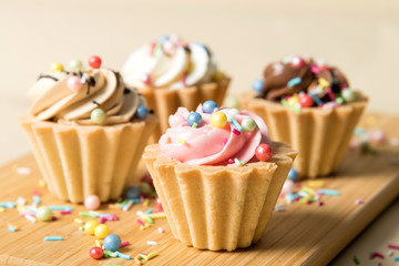 close-up of a sweet pastry dessert with multicolored cream and multicolored sprinkling on a wooden Board and a blurred light background