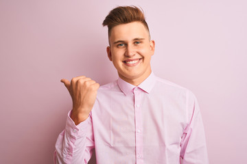 Young handsome businessman wearing elegant shirt standing over isolated pink background smiling with happy face looking and pointing to the side with thumb up.