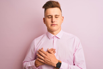 Young handsome businessman wearing elegant shirt standing over isolated pink background smiling with hands on chest with closed eyes and grateful gesture on face. Health concept.