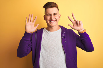 Young handsome man wearing purple sweatshirt standing over isolated yellow background showing and pointing up with fingers number eight while smiling confident and happy.