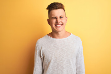 Young handsome man wearing white casual t-shirt standing over isolated yellow background winking...