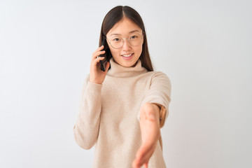 Young chinese woman talking on the smartphone over isolated white background smiling friendly offering handshake as greeting and welcoming. Successful business.