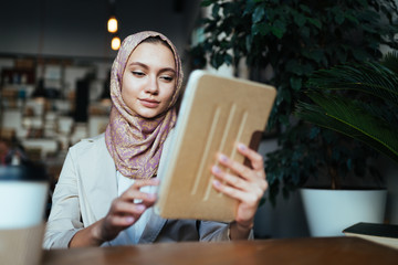 Muslim woman with emotion looks in a tablet pc while sitting in a cafe