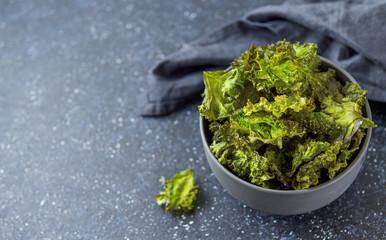 Green Kale Chips with salt in bowl. Homemade healthy snack for low carb, keto, low calorie diet. Dark blue background. Ready-to-eat kale chips, copy space left. Banner
