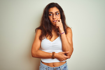 Young beautiful woman wearing t-shirt and glasses standing over isolated white background looking stressed and nervous with hands on mouth biting nails. Anxiety problem.