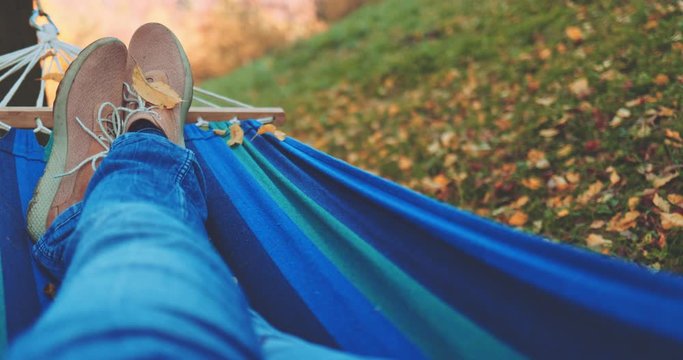 Unrecognizable Man Relaxes in a Hammock in Autumn. Point Of View, SLOW MOTION. POV: Male feet in comfortable shoes, person unwinds in a calm fall outdoor, rural forest landscape, cozy time in nature.