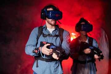 Man and woman using virtual reality headset and weapon in smoky space, red light of the playing club © alfa27