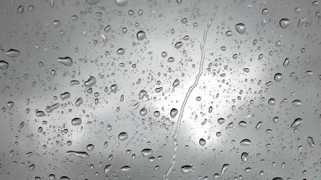 Close up view of water drops falling on glass. Rain running down on window. Rainy season, autumn. Raindrops trickle down, grey sky background