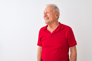 Senior grey-haired man wearing red polo standing over isolated white background looking away to...