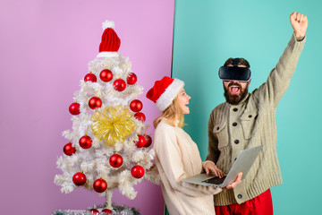 Excited bearded man in virtual 3D glasses. Woman in santa hat with laptop. 3d technology, virtual reality, entertainment. Virtual reality mask. New Year, Christmas, future and technology concept.