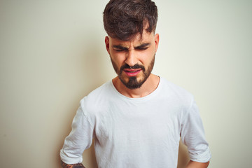 Young man with tattoo wearing t-shirt standing over isolated white background with hand on stomach because indigestion, painful illness feeling unwell. Ache concept.