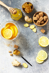 Hot cup of ginger tea and ingredients - lemon, ginger, honeycomb, honey on a gray stone countertop. Top view flat lay. Free space for your text.